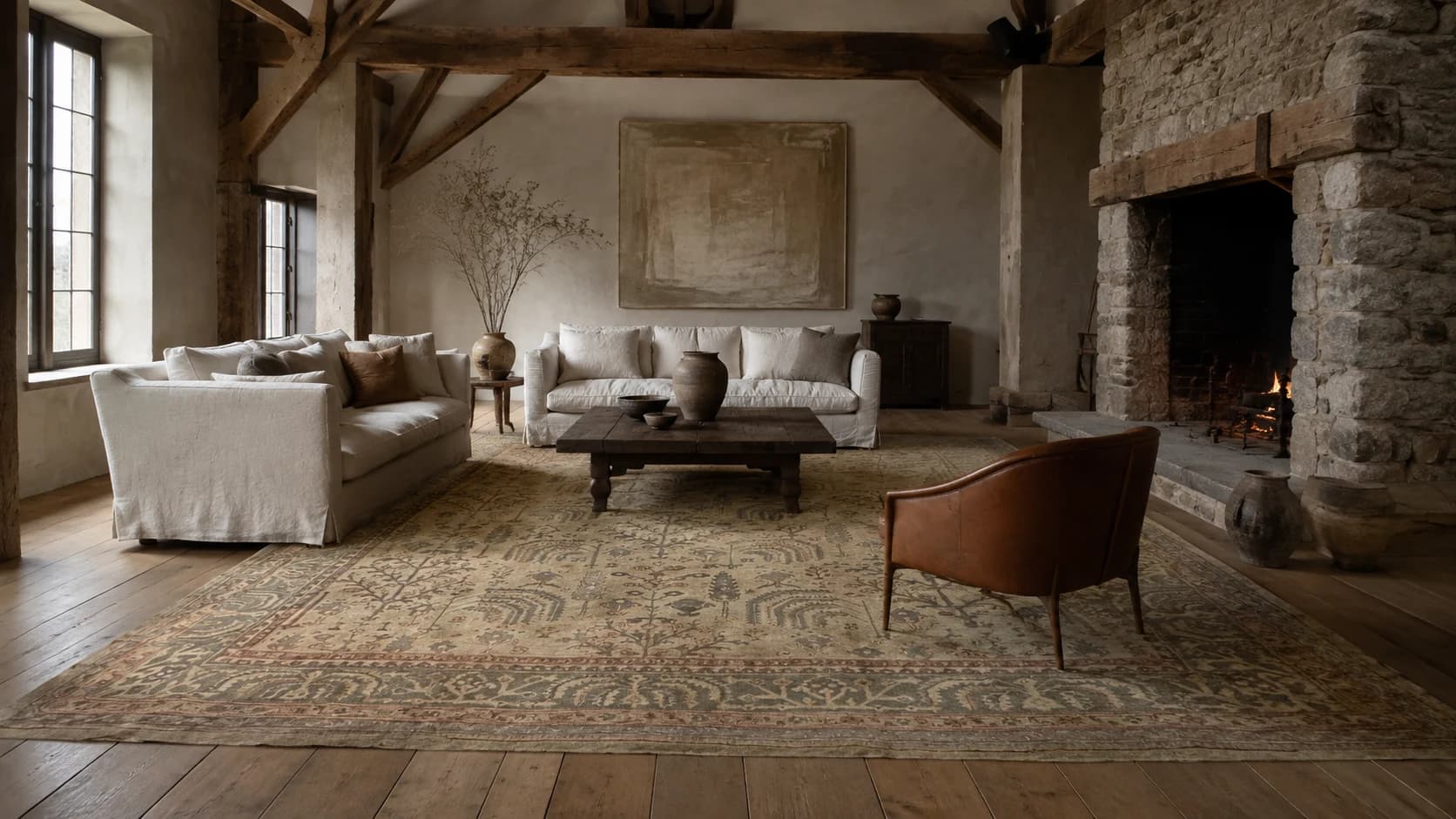 Large soft taupe Oushak rug grounding a living room with pale sofas and a stone fireplace